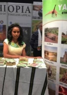Yama Ethiopia Tours team member at a tourism exhibition table displaying tour materials