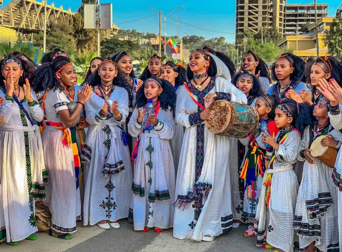 Girls in embroidered dresses and grass skirts dancing through the streets during Ashenda in Tigray, Ethiopia