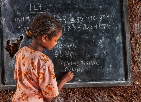 Young Ethiopian girl writing Amharic alphabet characters on a chalkboard