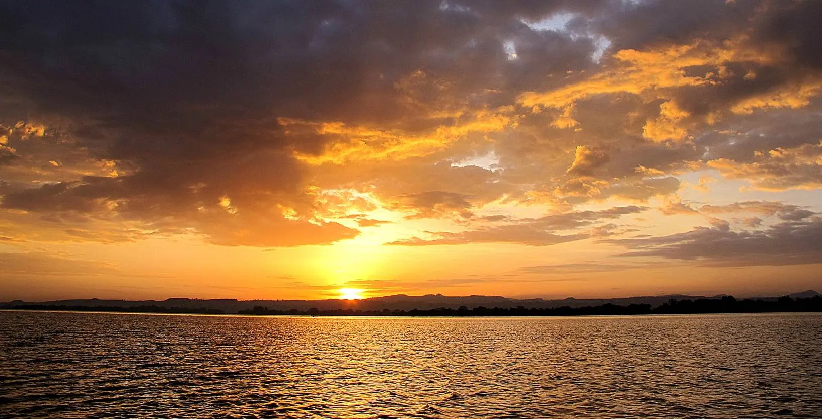 Dramatic golden sunset over a calm lake with storm clouds, Ethiopia