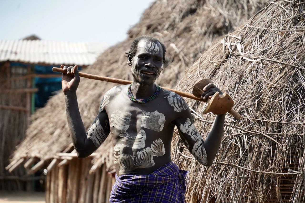 Karo man with traditional body paint carrying a wooden headrest and stick