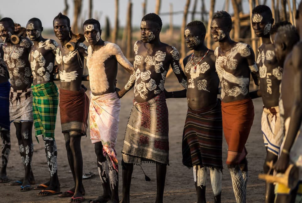Karo men with traditional body paint carrying wooden headrests and sticks