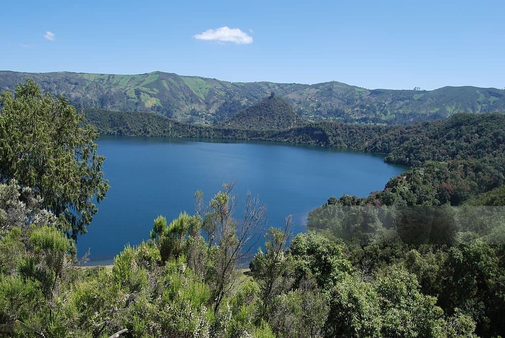 Blue crater lake framed by forested mountains and hills