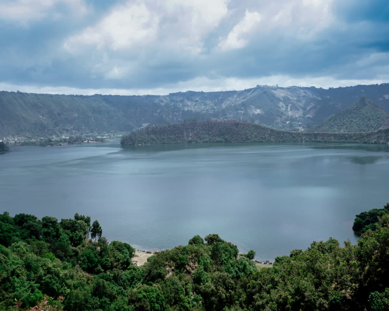 Wenchi crater lake surrounded by misty green mountains under a cloudy sky