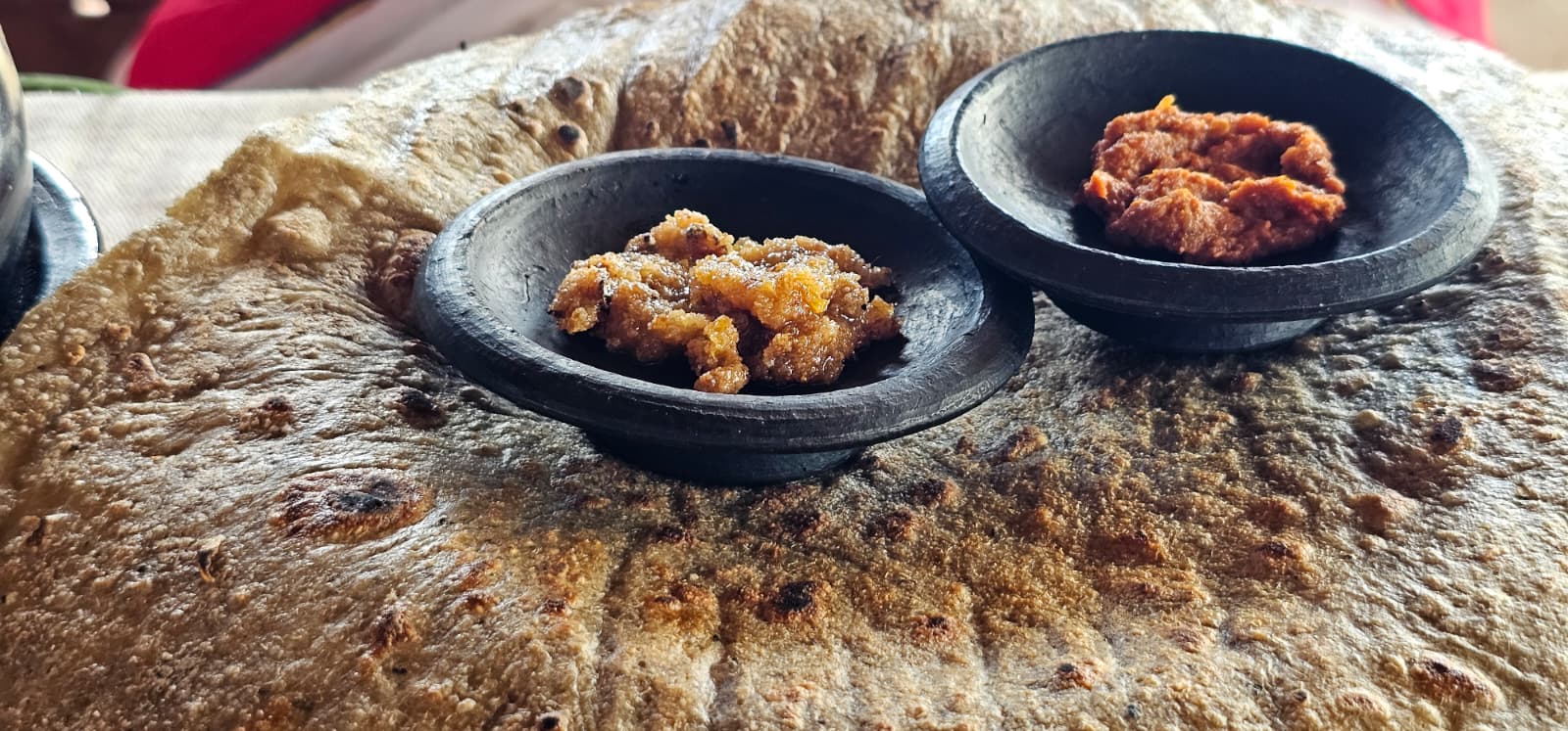 Large toasted enset flatbread served with two black clay bowls of golden and spiced chili dips in a Dorze village, Gamo Highlands, Ethiopia