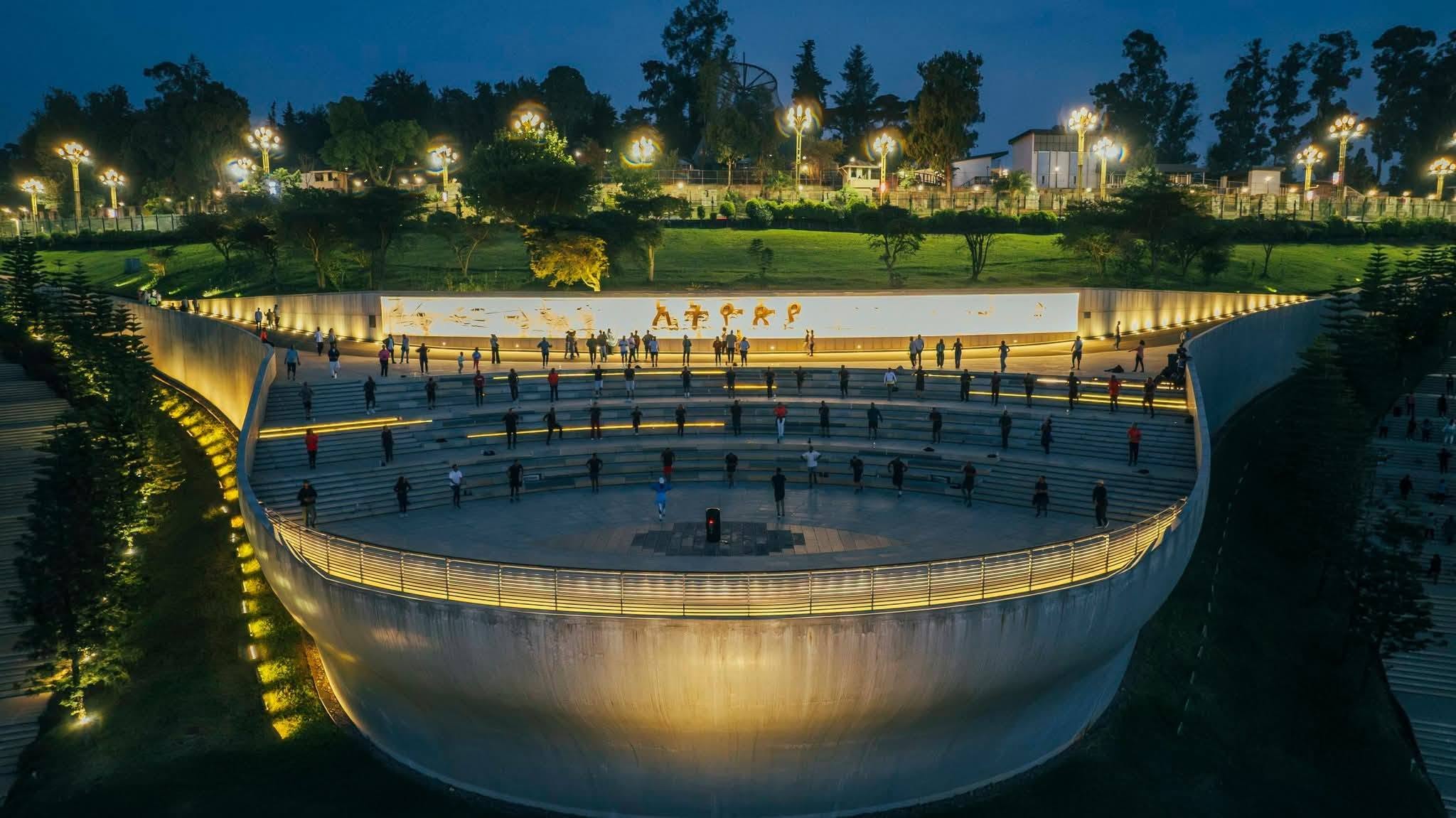 The illuminated amphitheater at Friendship Park at dusk with people gathered and the Ethiopia wall glowing