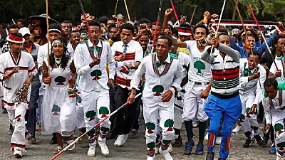 Youth walking in joyful Irreecha procession wearing white ceremonial attire and singing festive chants