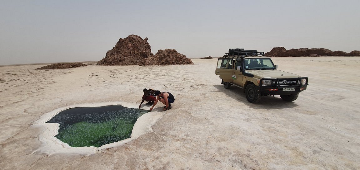 Travelers examining a mineral-green salt pool beside a 4x4 vehicle in the Danakil Depression