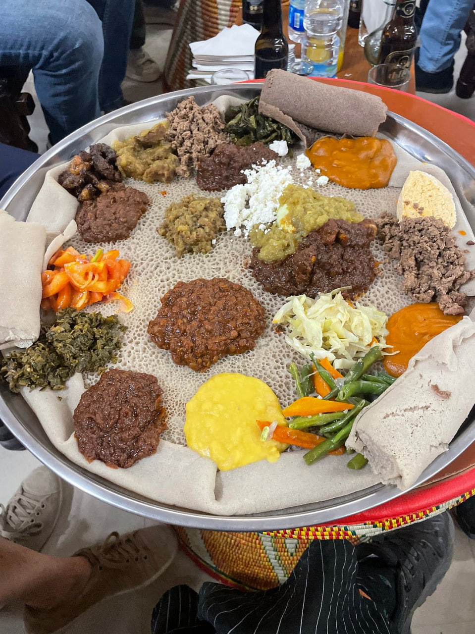 Traditional Ethiopian injera platter with assorted wat stews, vegetables, and cheese