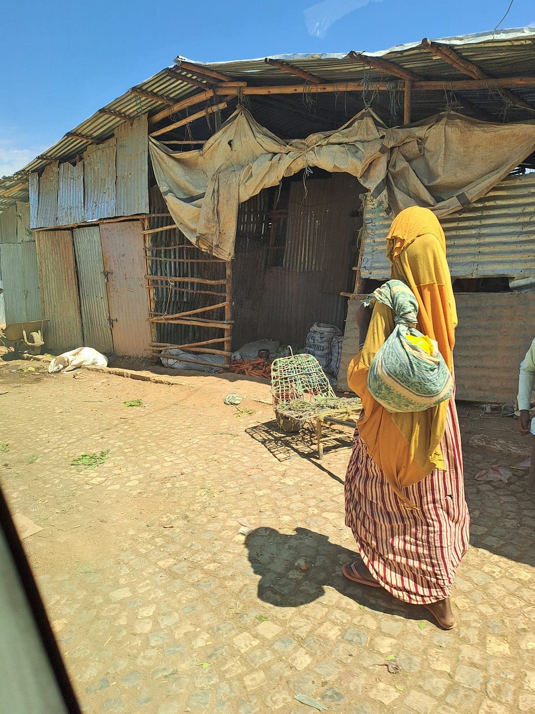 Woman in traditional yellow dress walking past a market stall, Ethiopia