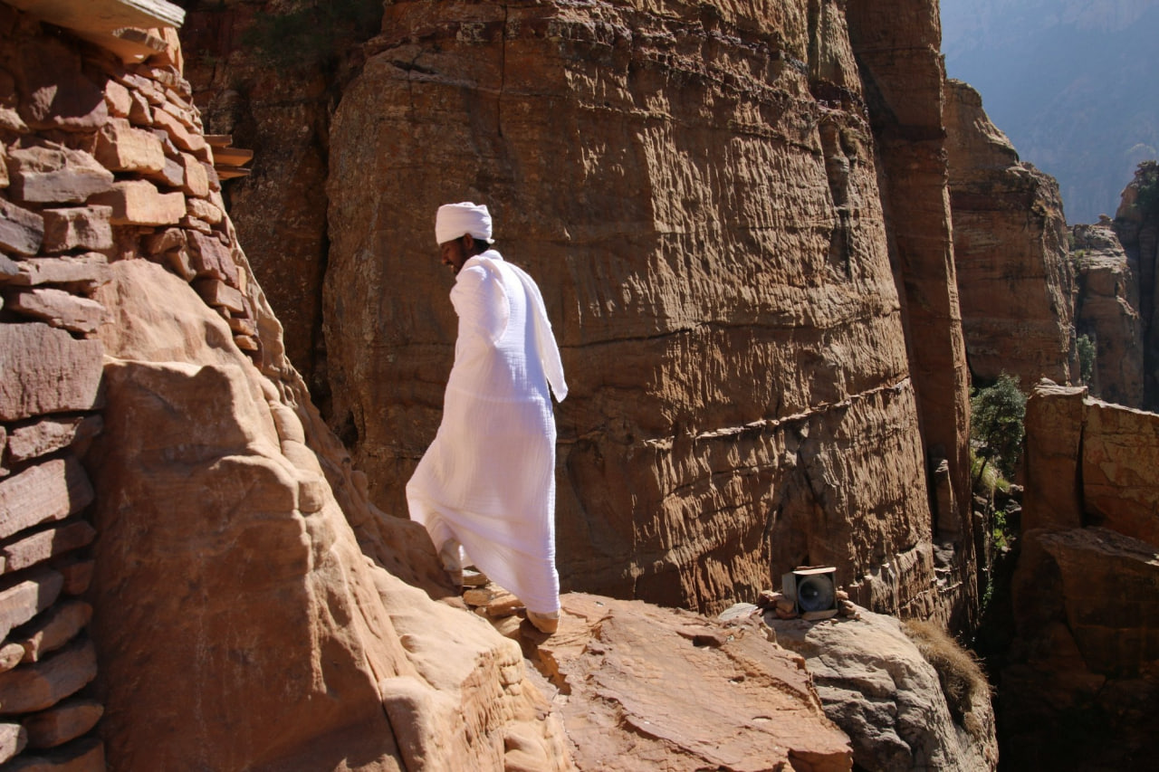 Ethiopian Orthodox priest in white robes walking a cliffside path to a Tigray rock church