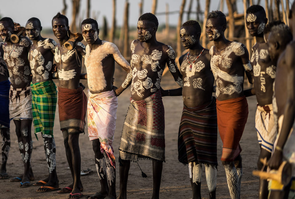 Karo men with traditional body paint carrying wooden headrests and sticks