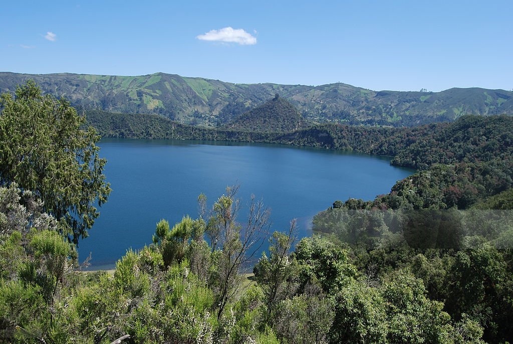 Blue crater lake framed by forested mountains and hills