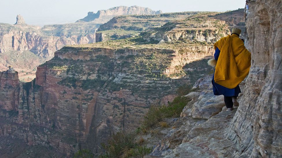 Priest in traditional robes walking a cliffside path in the Gheralta Mountains, Ethiopia