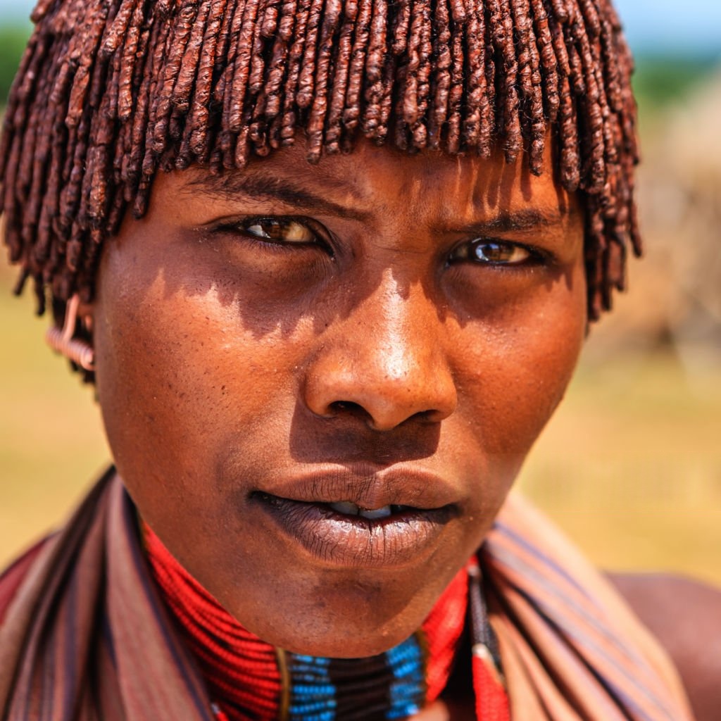 Close-up portrait of a Hamar tribeswoman with traditional ochre-coated braided hair and beaded necklace, southern Ethiopia
